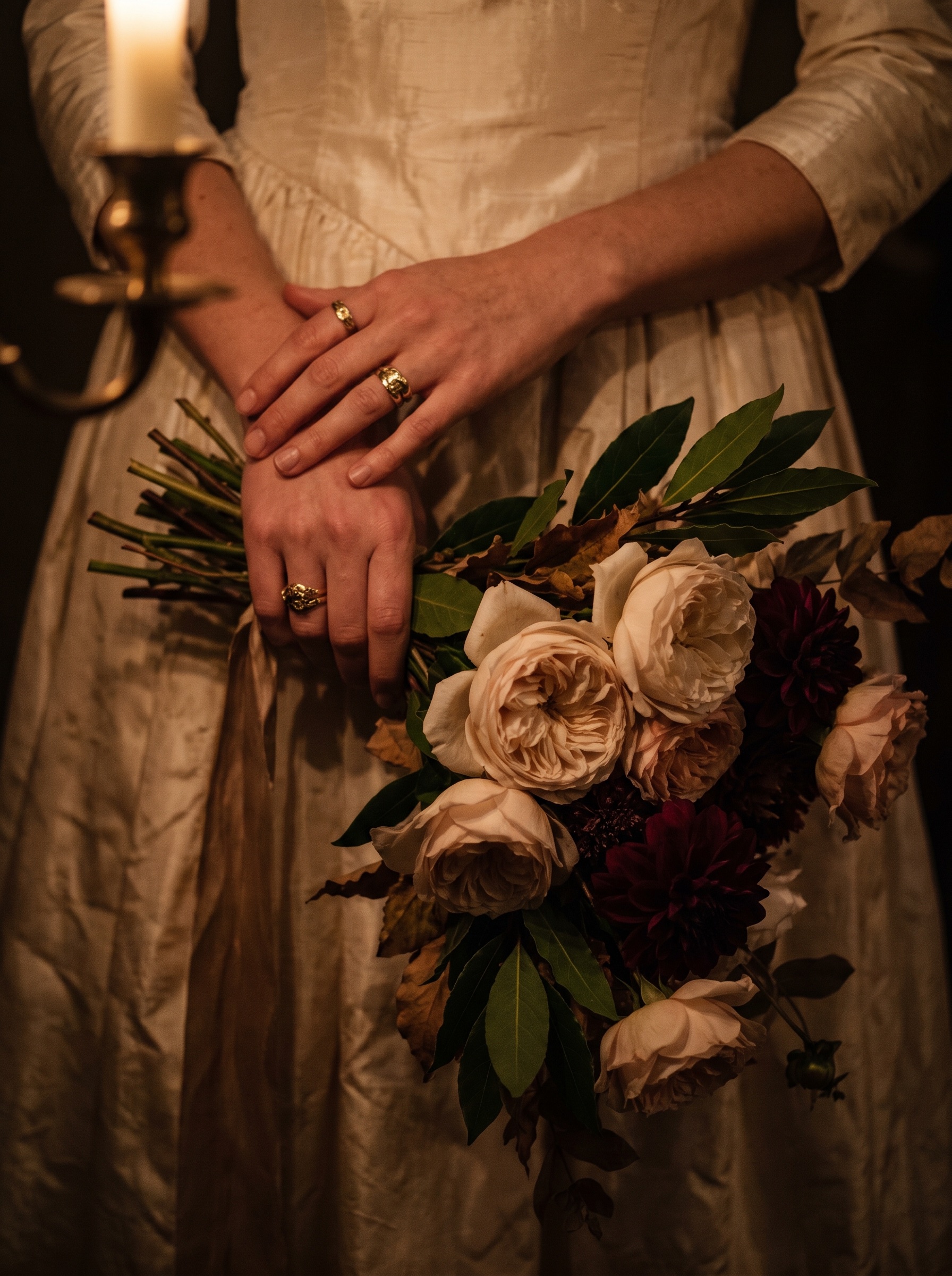 A bride’s hands holding a loose bouquet of garden roses in candlelight