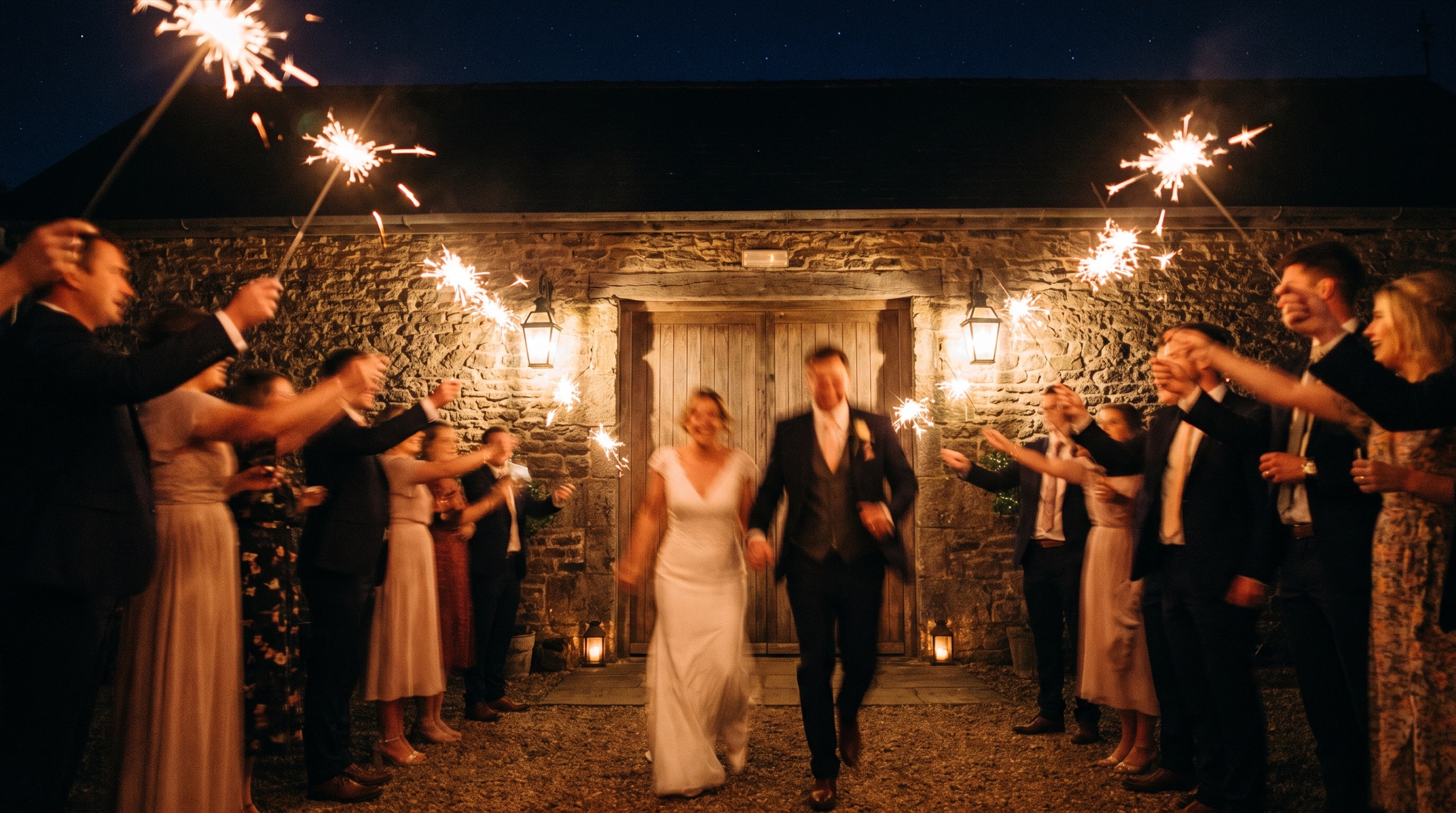 Wedding guests forming a corridor of held sparklers for the couple’s departure at night